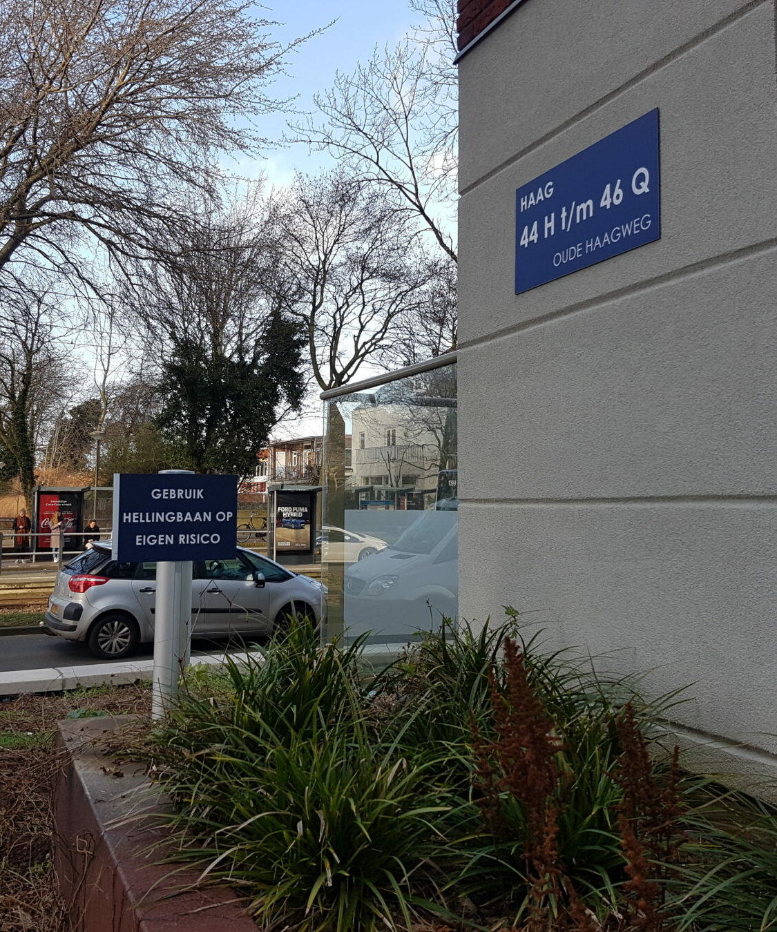 Blauwe gevelplaat met straatnaam en blauw infobord op staander buiten naast gebouw